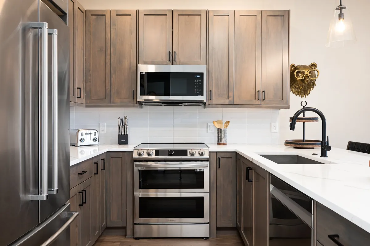 A contemporary kitchen with stainless steel appliances, white countertops, warm wooden cabinets, and a decorative animal head. The space is set up for cooking and family meals, with a welcoming, functional layout ideal for preparing large feasts or casual breakfasts.