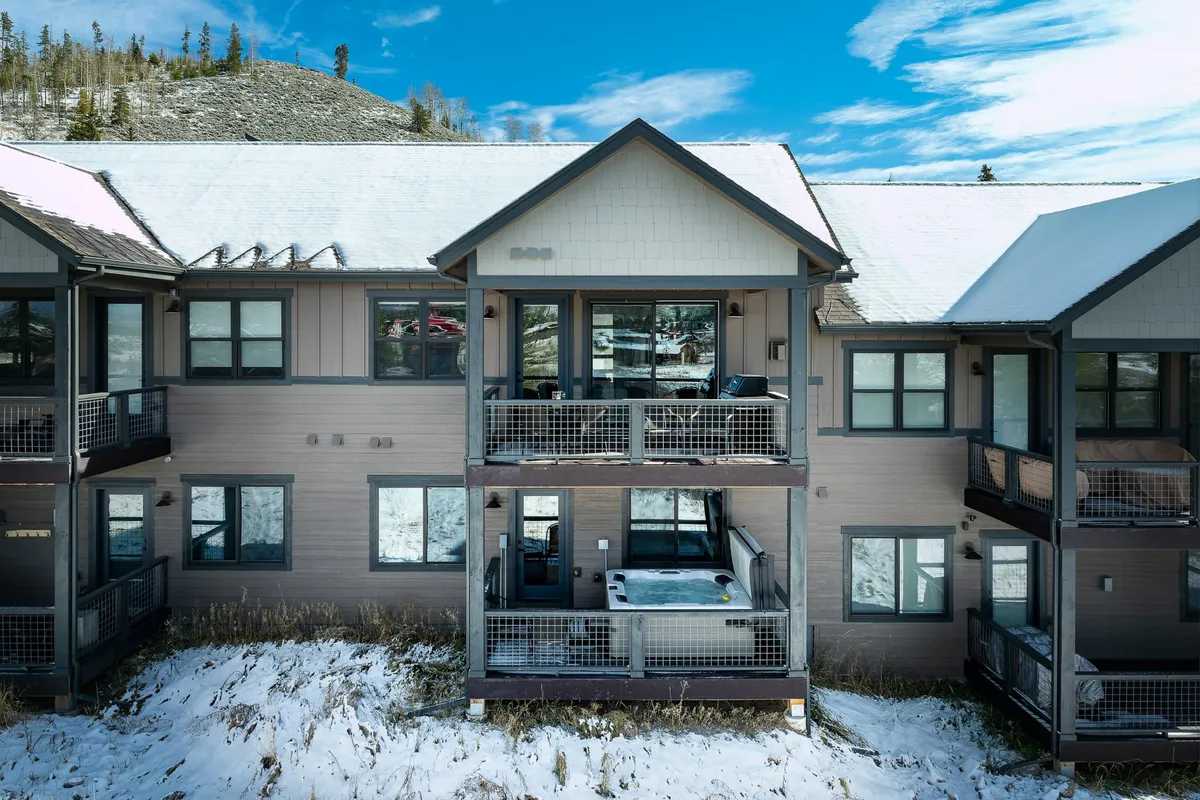 A private balcony featuring a bubbling hot tub overlooks a snow-blanketed ground with majestic mountains in the distance. The cozy setting is perfect for unwinding after an active day, offering both relaxation and breathtaking views.