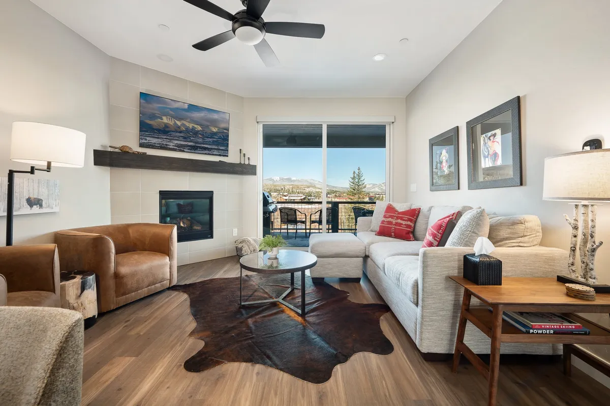The image showcases a cozy living area with a crackling fireplace as the focal point, surrounded by plush sofas adorned with red pillows. Sunlight pours in through expansive windows, offering breathtaking views of the Colorado landscape. The inviting coffee table and comfortable seating create the perfect space for family gatherings, relaxing evenings, or lively game nights.