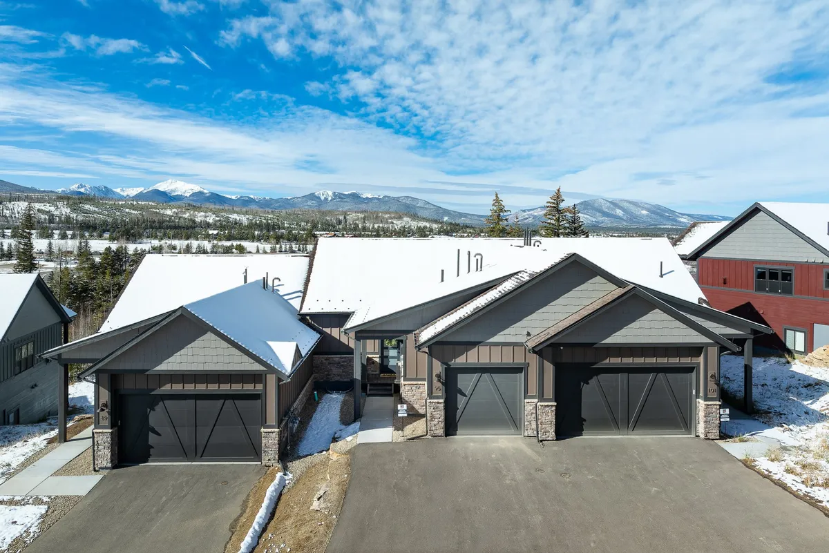 A modern chalet with snow-capped roofs set against a majestic mountain backdrop, epitomizing the allure of a luxurious mountain escape. The exterior highlights the property's impressive architecture and its seamless integration with the surrounding wilderness.