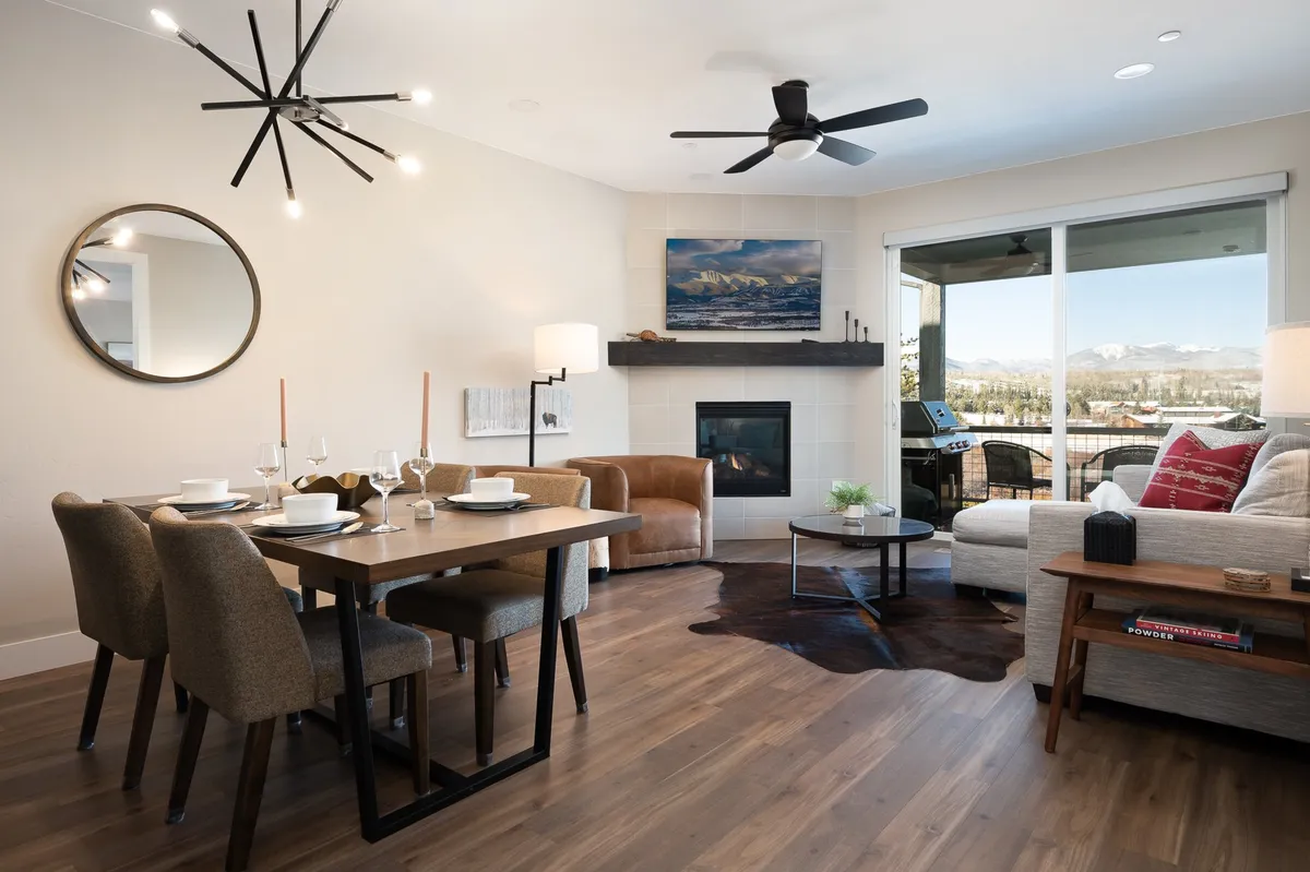 An open-concept living space blending a dining area, fireplace, sofa, and a large window framing a striking mountain view. The inviting setting encourages socializing and relaxation, while the fire adds a warm, cozy ambiance ideal for memorable moments.