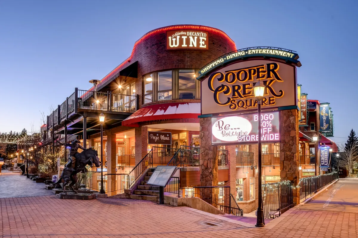 A lively exterior scene at Cooper Creek Square, featuring visible signage for shopping, wine tasting, and a welcoming staircase. The area buzzes with the promise of dining, entertainment, and boutique experiences close to the property.