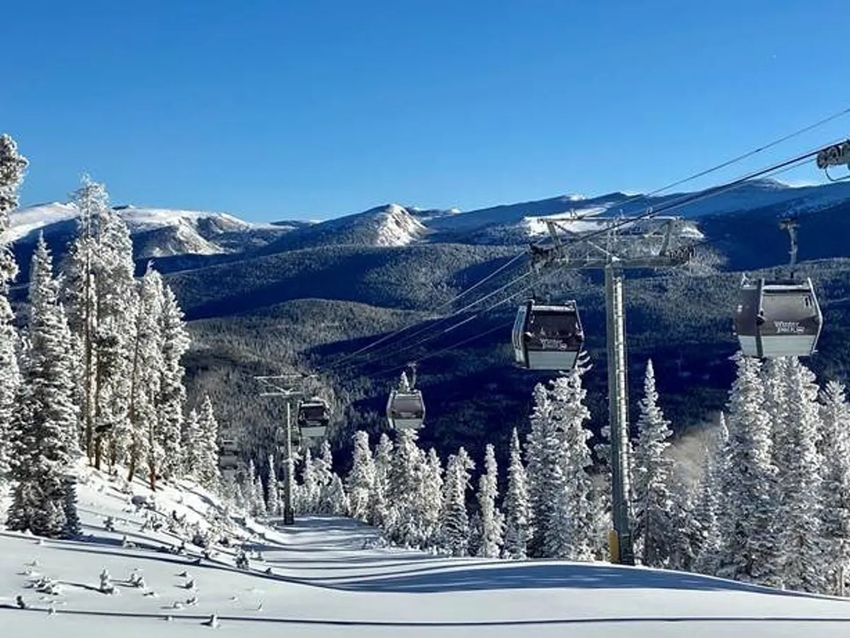 This image captures ski lift gondolas gliding above a snow-covered landscape, framed by pine trees and a dramatic mountain range. The scene is vibrant with activity, with the lifts ascending toward the slopes, inviting viewers to imagine themselves embarking on a day of skiing or snowboarding.